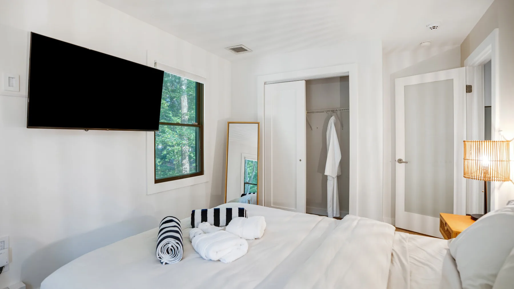 Un dormitorio luminoso con una cama grande, un televisor en la pared y una ventana.