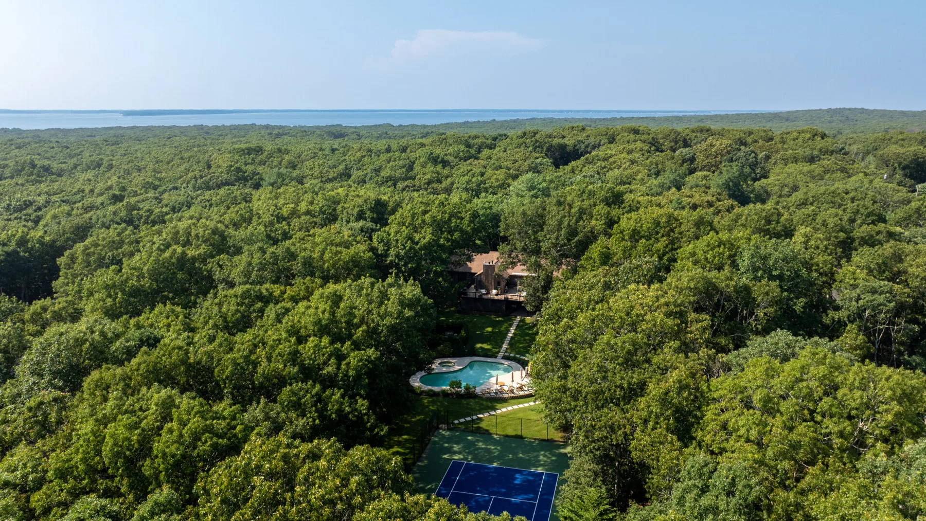 Vista aérea de un paisaje boscoso con piscina y cancha de tenis.