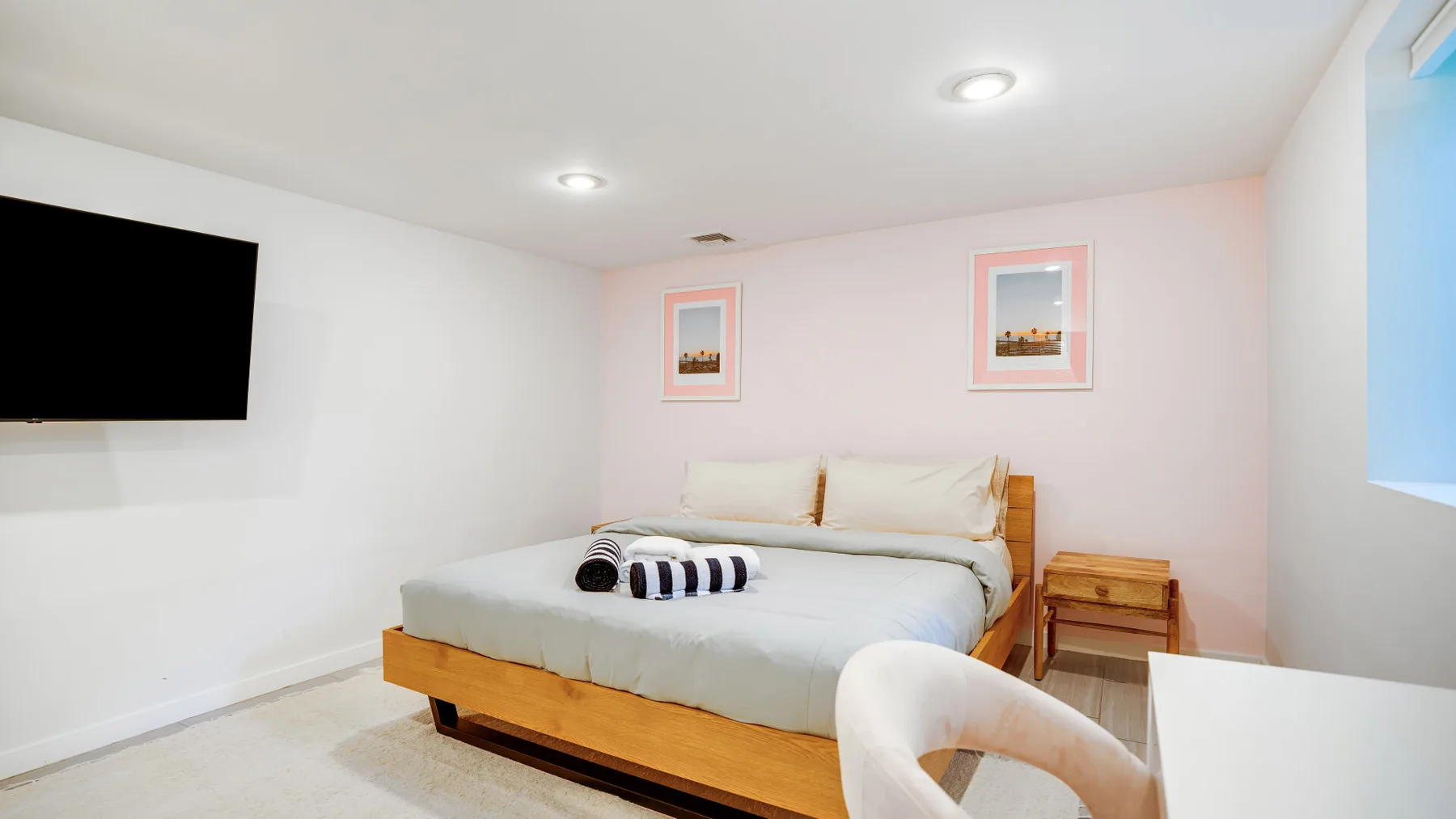 Un dormitorio con una cama, un televisor montado en la pared y una mesita de noche.