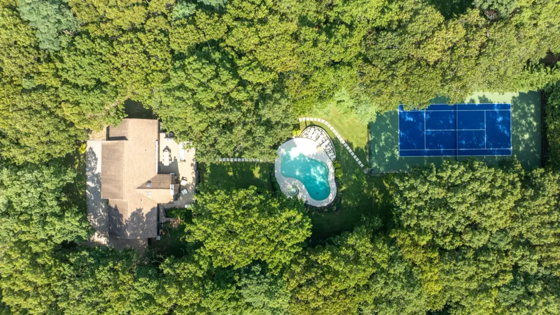 Una vista aérea muestra una casa, una piscina y paneles solares rodeados de árboles.