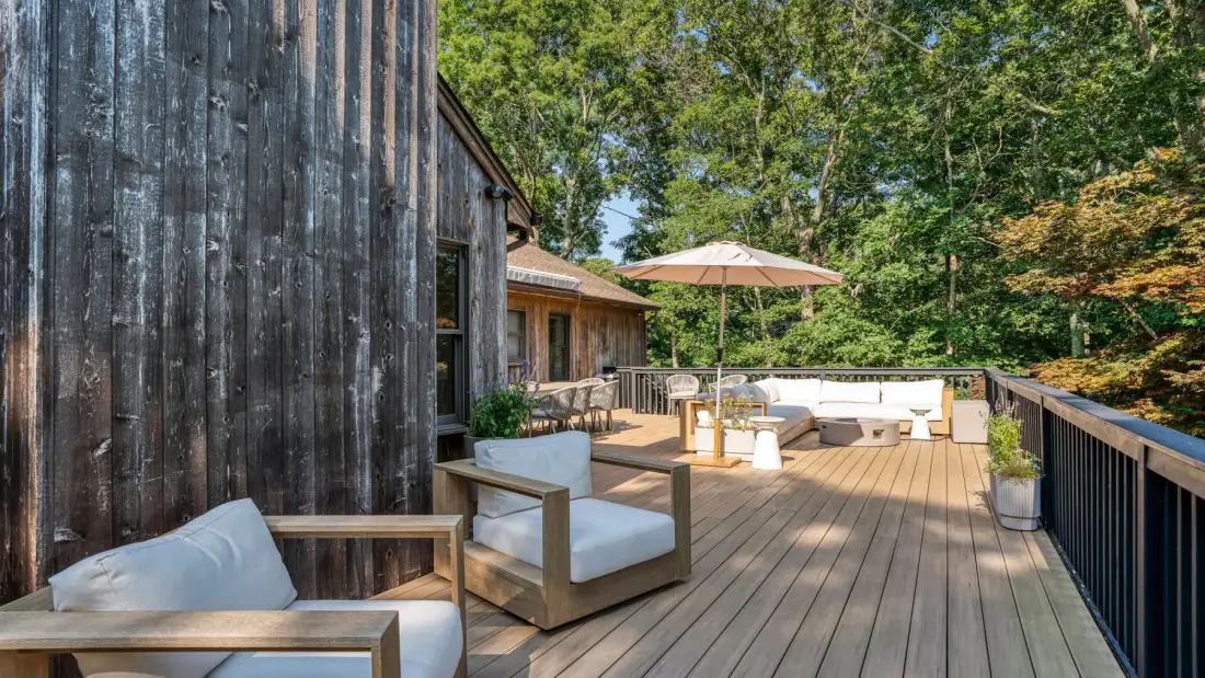 Una terraza de madera junto a una casa tiene asientos al aire libre y una sombrilla.