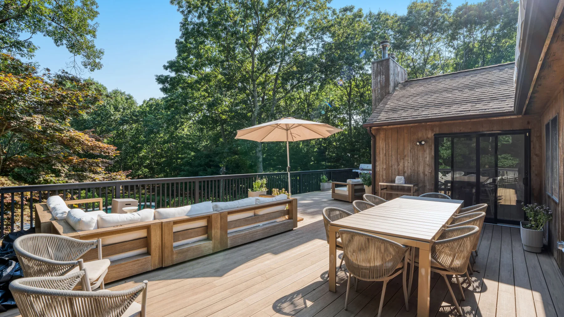 Una terraza de madera con asientos y una mesa de comedor da a un paisaje arbolado.