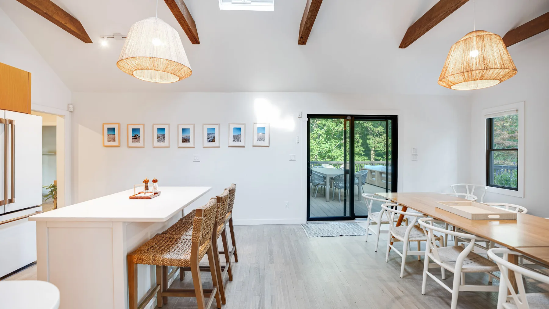 Un comedor luminoso con una mesa larga, asientos tejidos y puertas de vidrio.