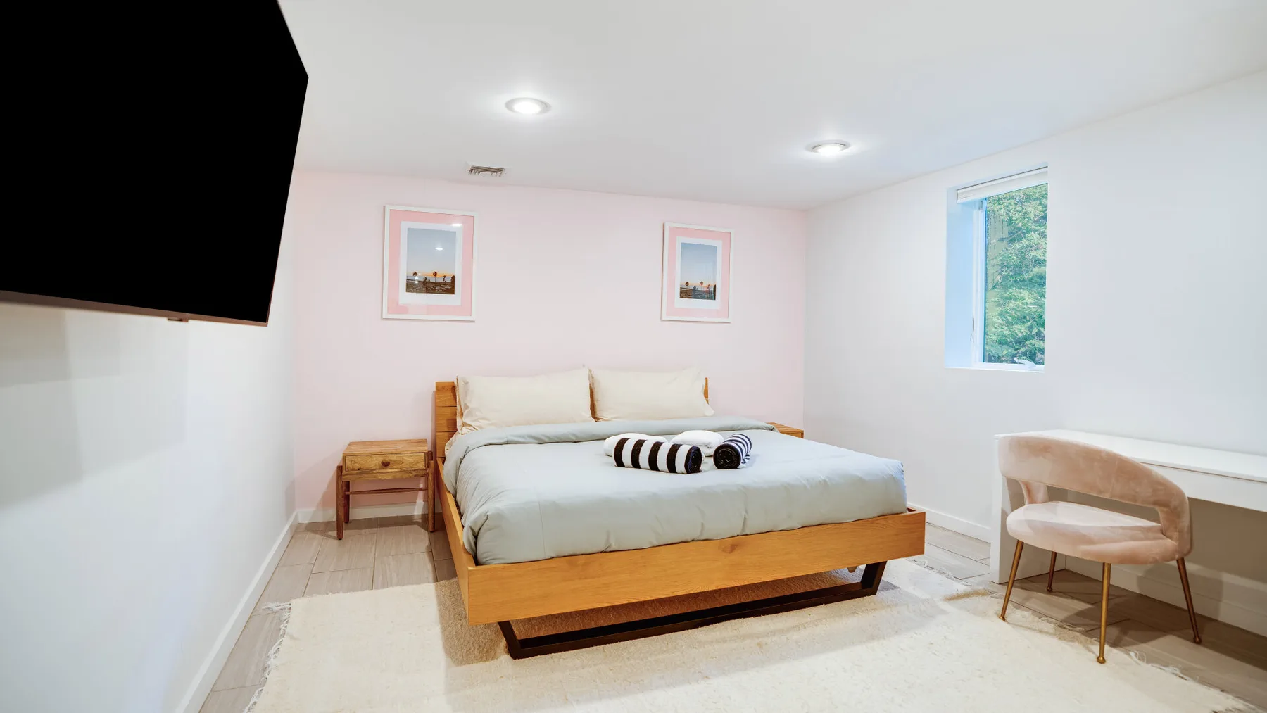 Un dormitorio luminoso con una cama baja, cuadros enmarcados y una ventana.