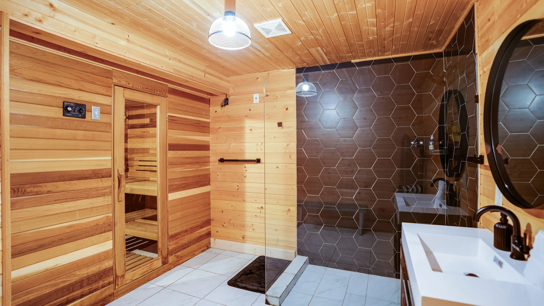 Un baño revestido de madera con una ducha de vidrio y un lavabo.