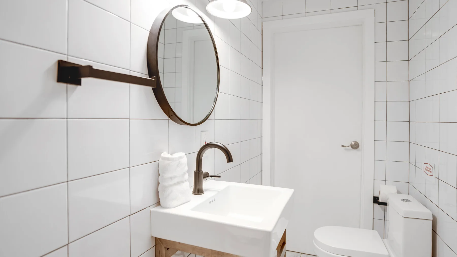 Un baño con azulejos, lavabo, espejo redondo e inodoro.