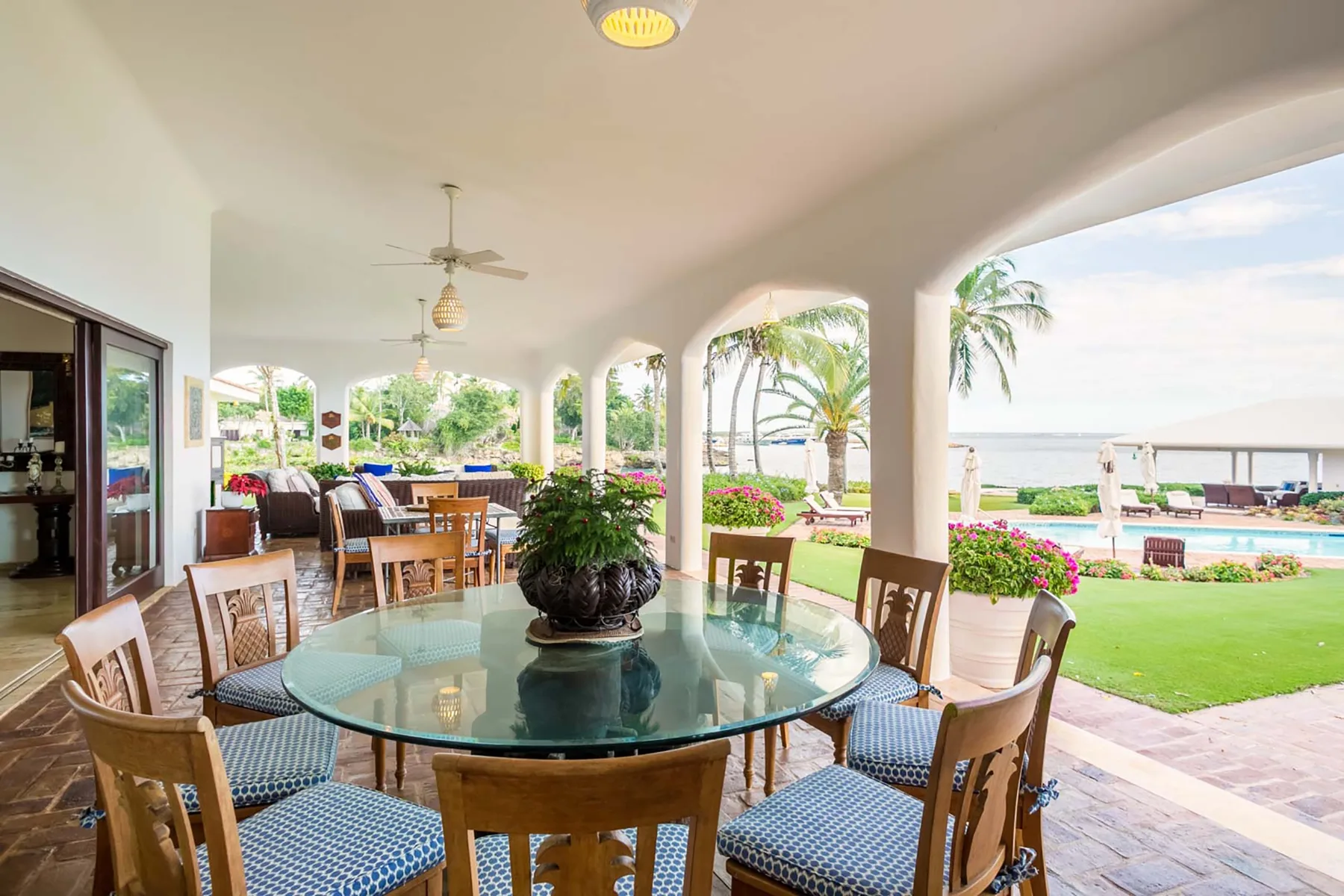 A covered patio dining area overlooks a lawn, pool, and water.