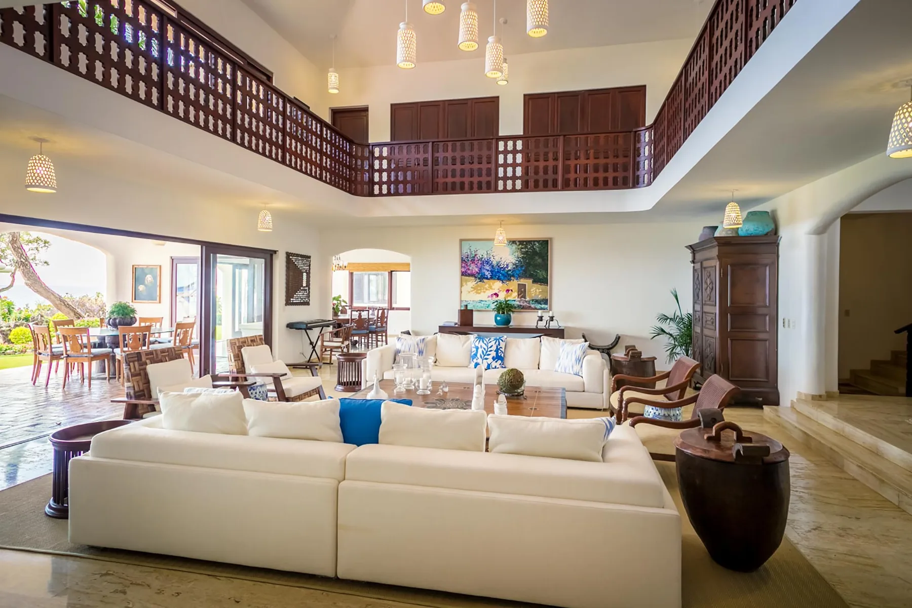 A spacious living room with seating beneath a dark wooden balcony railing.