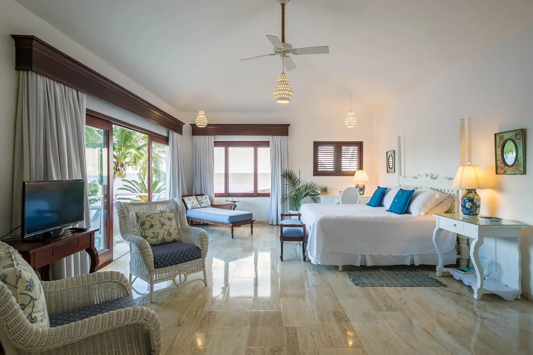 A bright bedroom with a large bed, seating, and windows overlooking greenery.