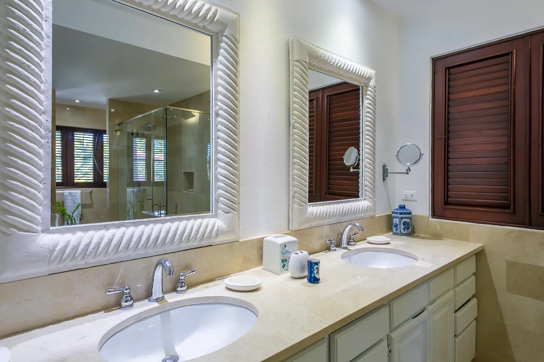 A bathroom vanity with sinks, framed mirrors, and dark wooden shutters.