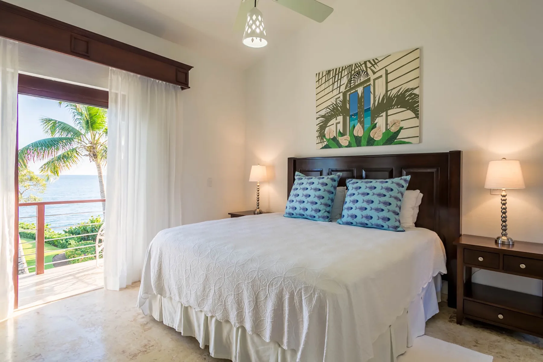 A bright bedroom with a neatly made bed and a view of palm trees through the balcony door.