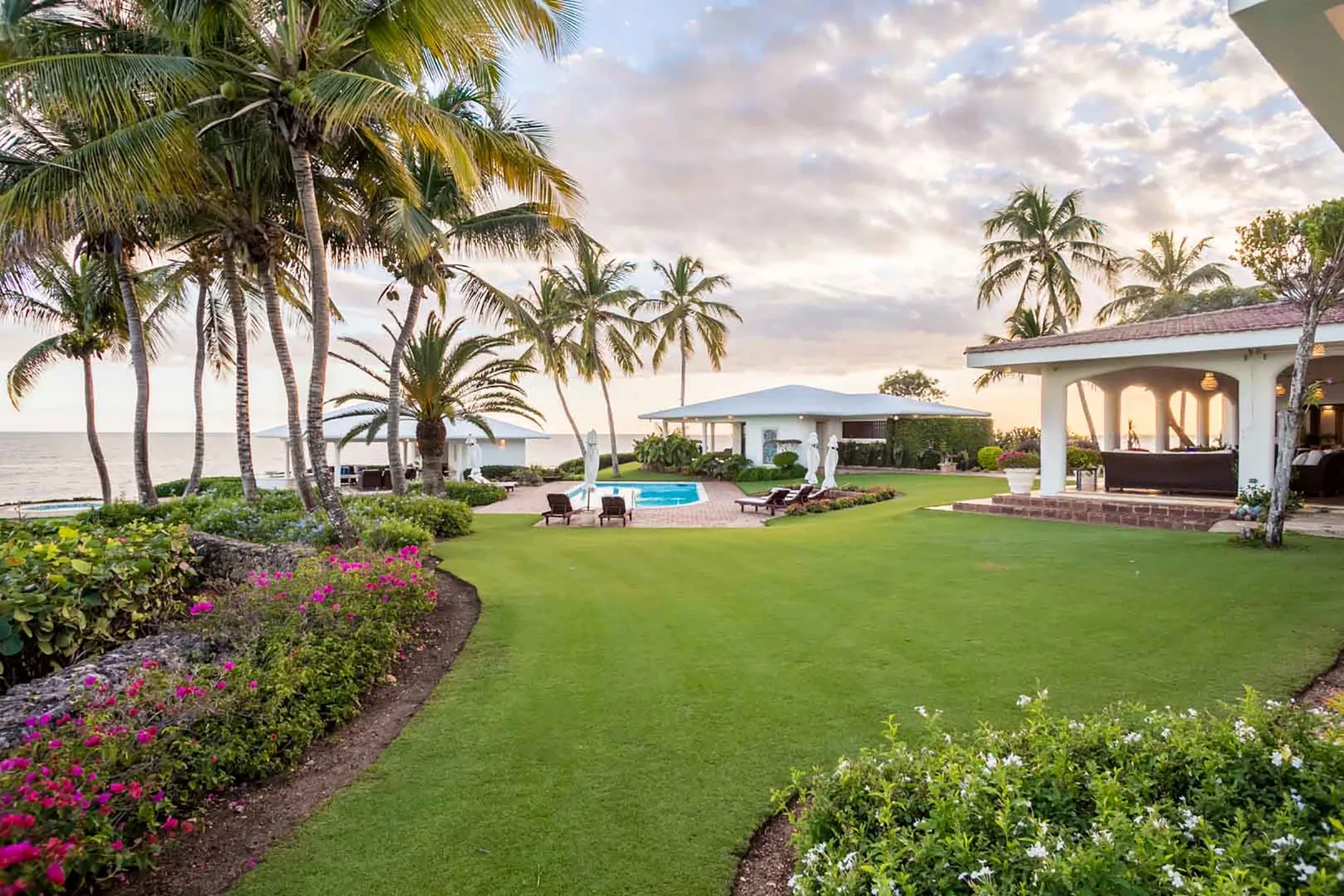 A landscaped tropical garden with palm trees, a pool, and the ocean beyond.