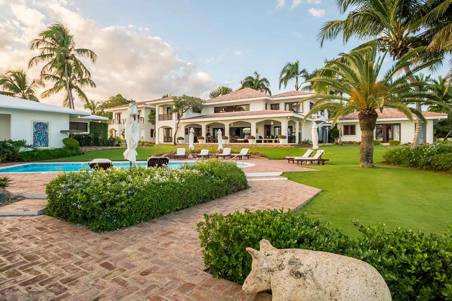 A large villa overlooks a landscaped lawn, pool, and paved patio.
