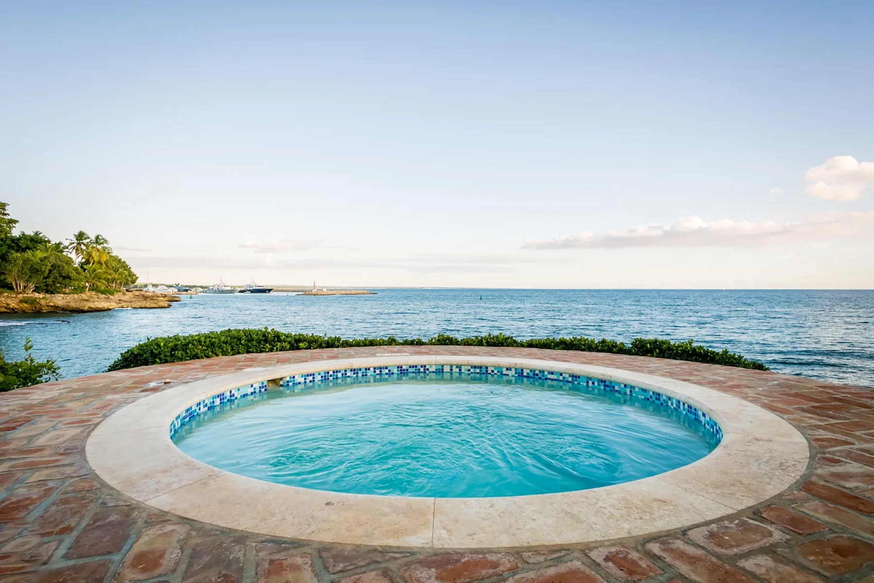 A round swimming pool sits beside the ocean, with a paved deck around it.