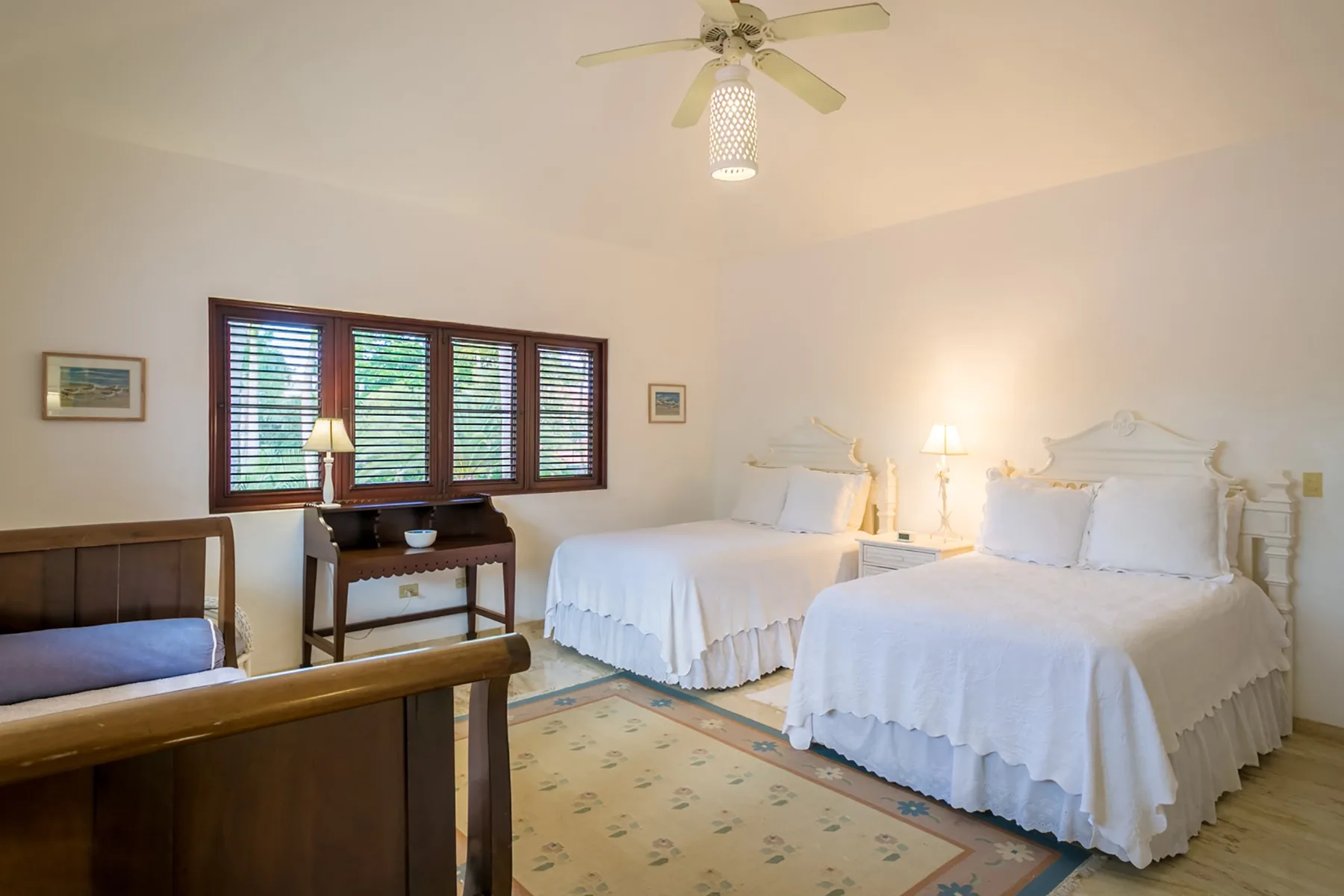 A bright bedroom with two beds, a window, and a ceiling fan.