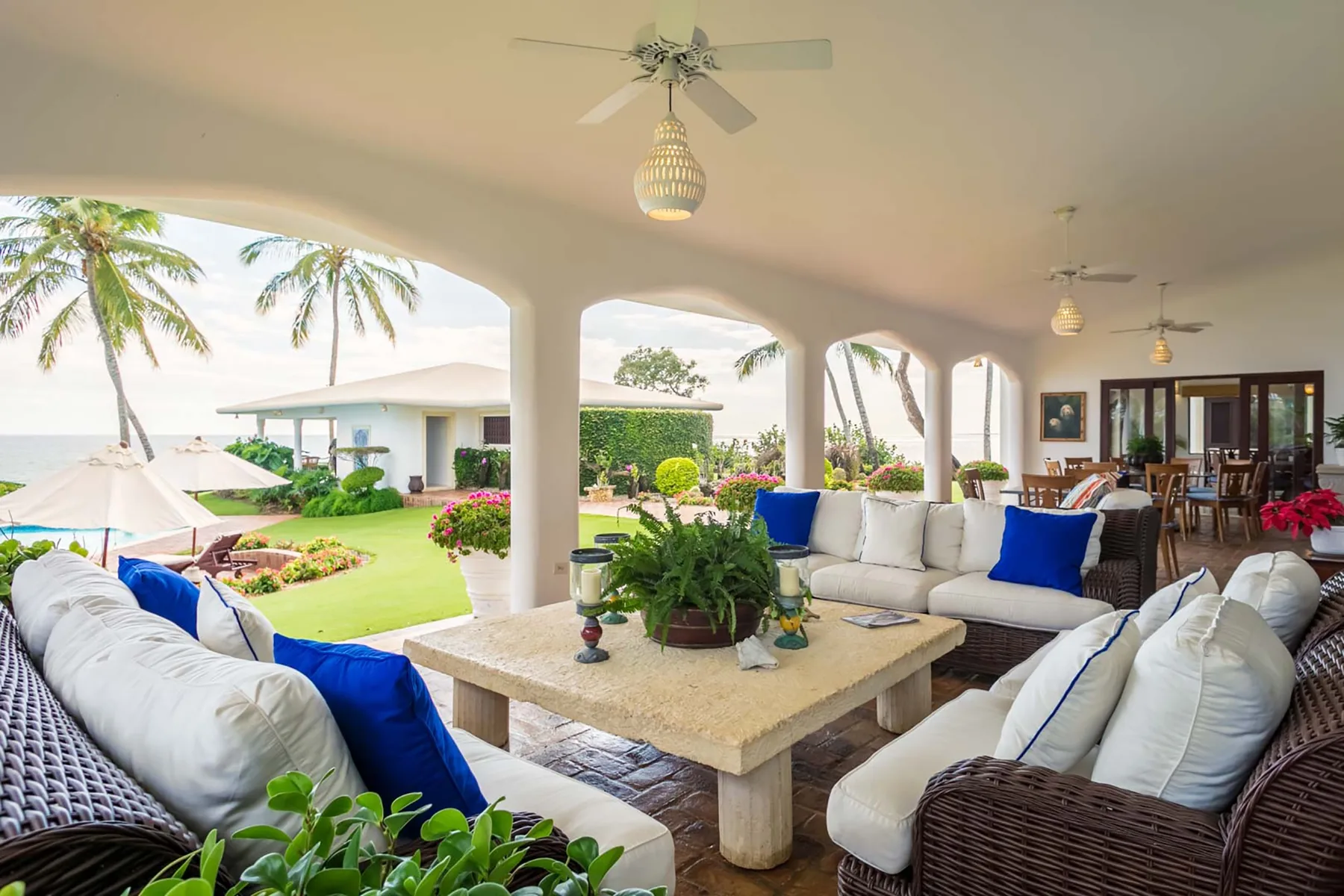 A covered outdoor lounge with cushioned seating and a view of the garden.