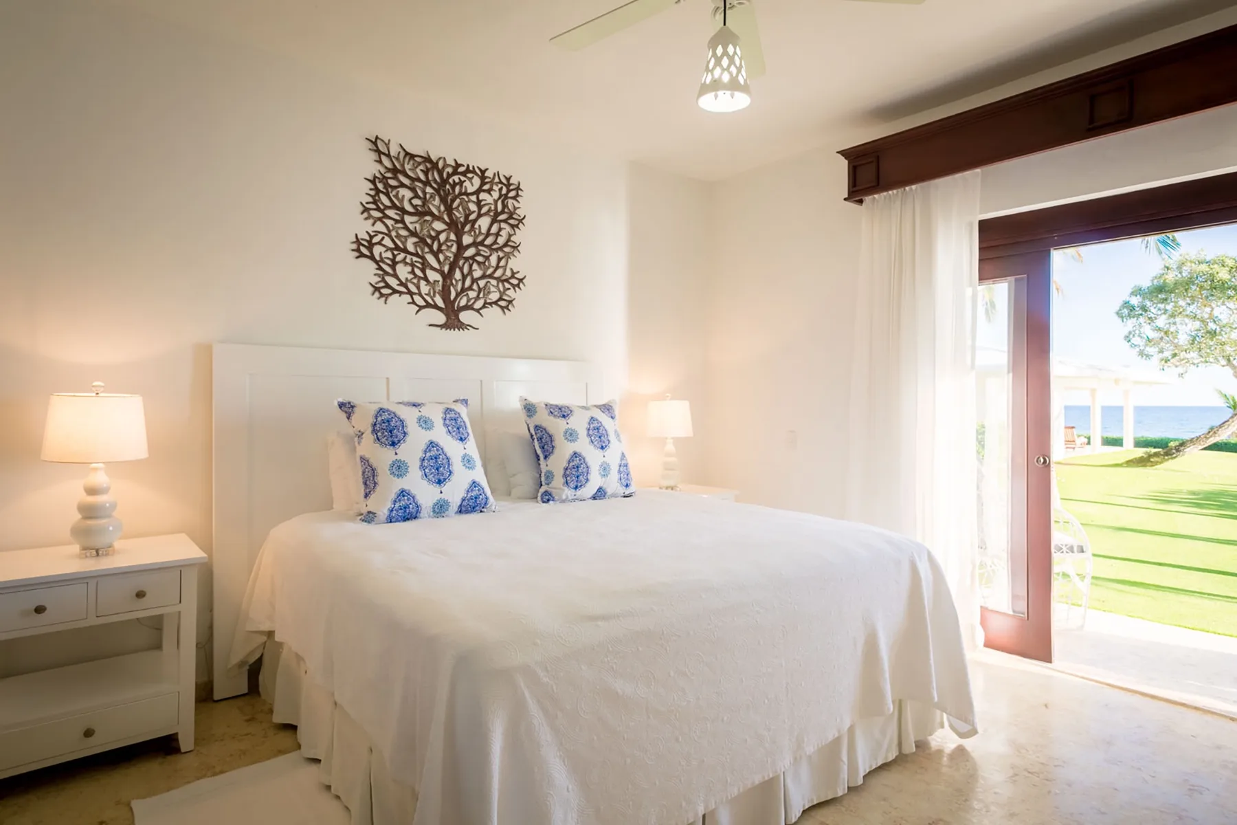 A bright bedroom with a white bed and an open doorway to a green lawn.