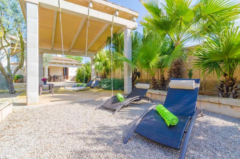 Un patio al aire libre con asientos de descanso bajo una pérgola cubierta, rodeado de palmeras.