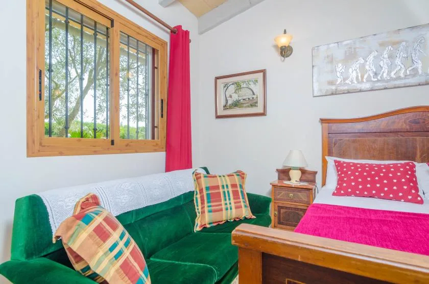 Un dormitorio con una zona de asiento verde junto a una cama y una ventana con rejas.