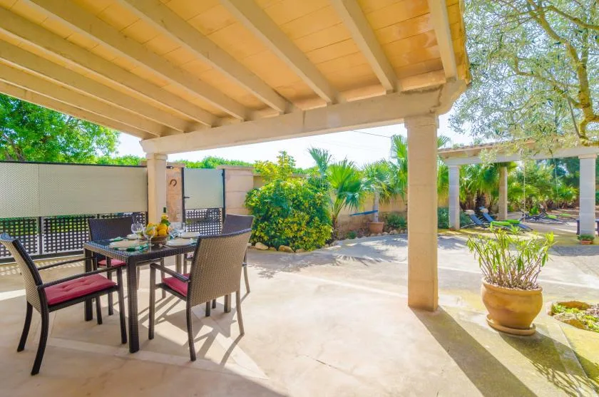 Un patio exterior sombreado con una mesa de comedor y plantas frondosas.