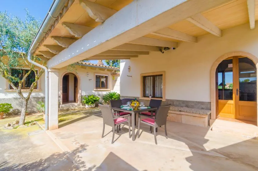 Una zona exterior cubierta para comer, con una mesa y asientos junto a la casa.