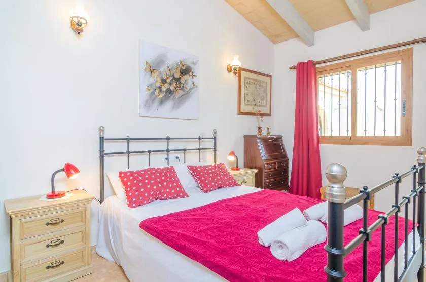 Un dormitorio con una cama de metal, ropa de cama rosa intenso y una ventana con cortinas rojas.