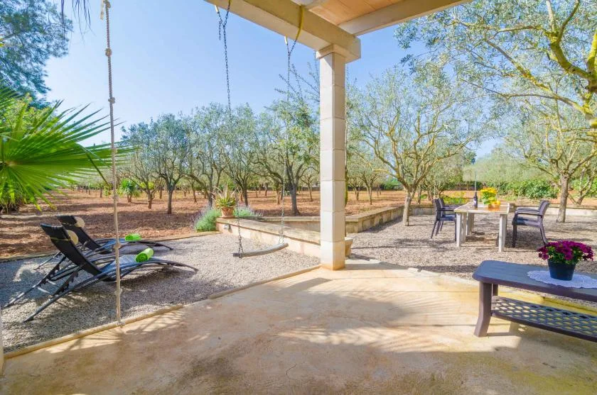 Un patio cubierto da a un jardín, con asientos al aire libre y un columpio colgante.