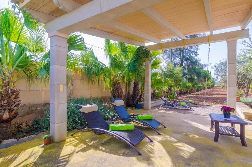 A covered outdoor patio with reclining lounge chairs and tropical plants.