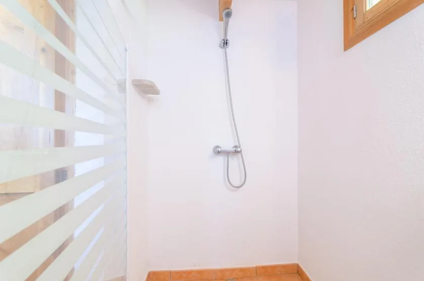 Una zona de ducha luminosa con cabezal de ducha en la pared y suelo de baldosas.