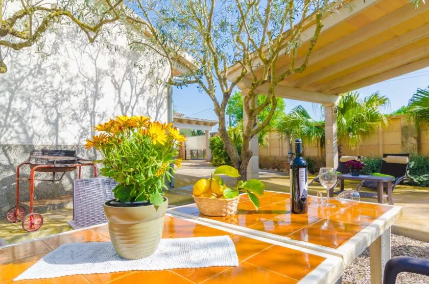 Una zona de comedor exterior iluminada por el sol, con una mesa de madera bajo una pérgola.