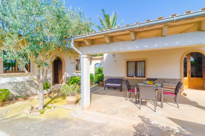 Un patio exterior sombreado con una mesa de comedor y asientos junto a una casa.
