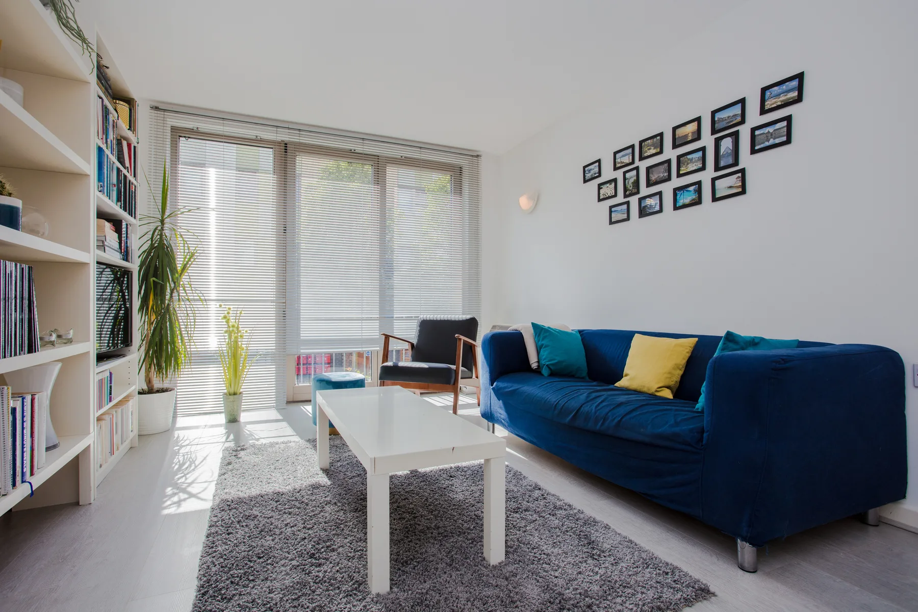 A bright living room with a blue sofa, white coffee table, and large windows.