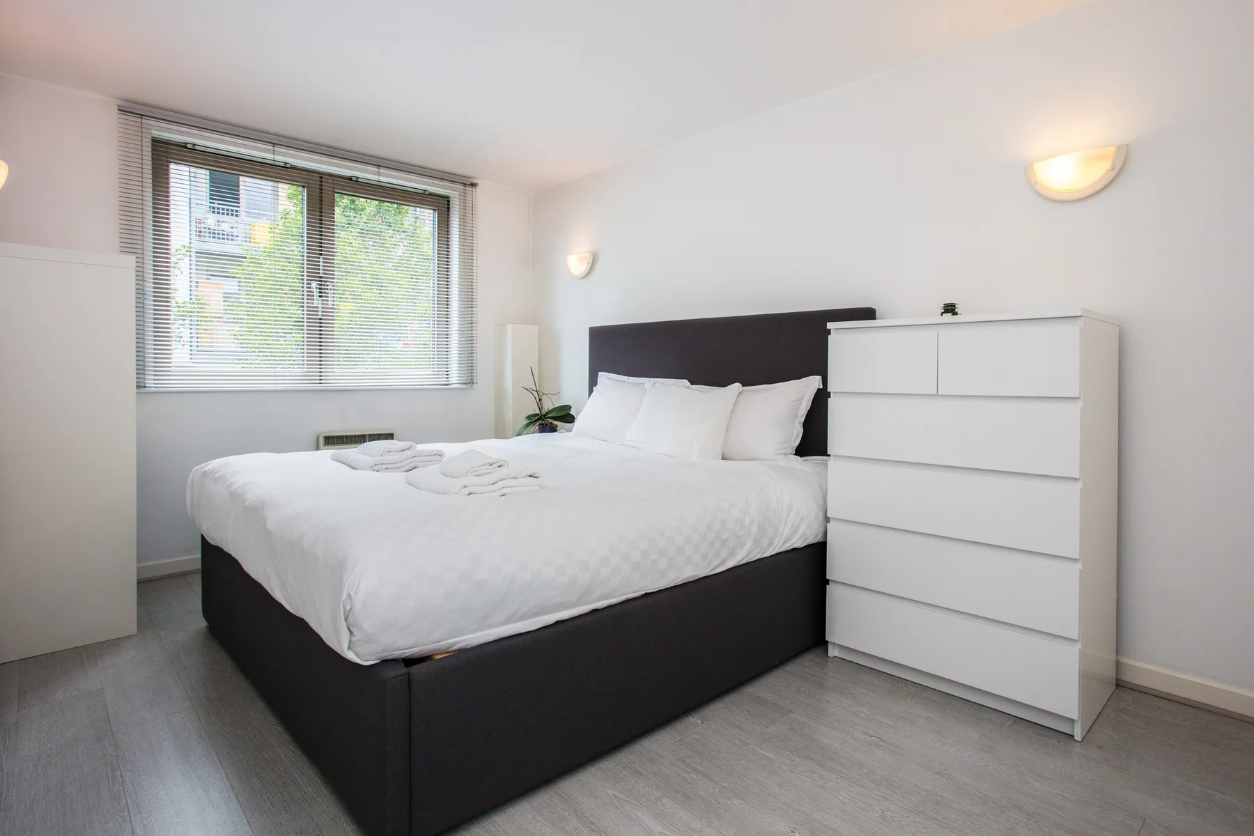 A bedroom with a neatly made bed beside a window.