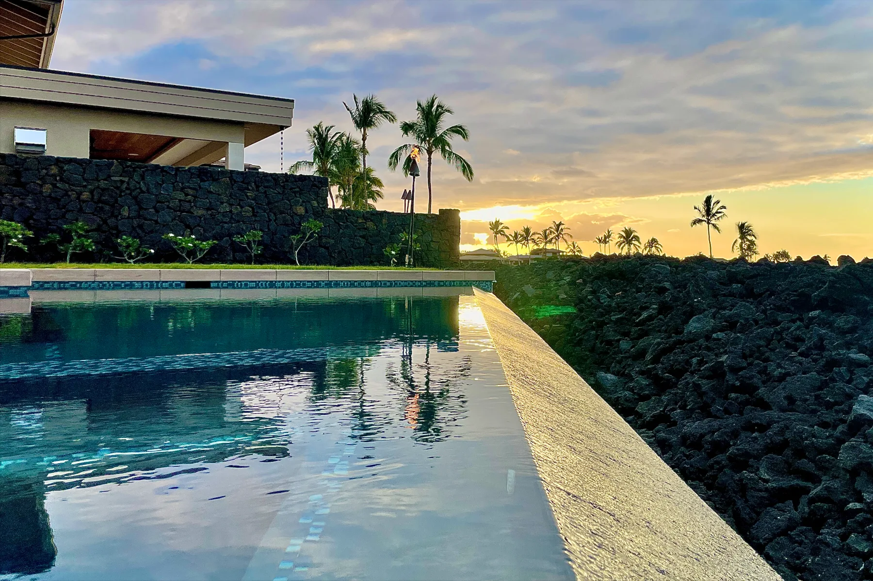 An outdoor swimming pool overlooks a rocky shoreline at sunset.