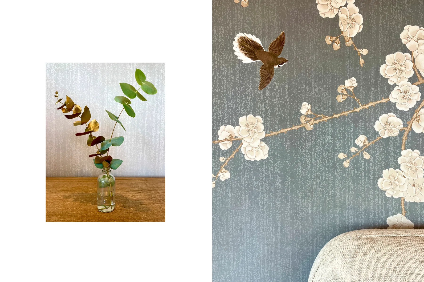A leafy branch in a glass bottle sits on a wooden surface beside floral wallpaper.