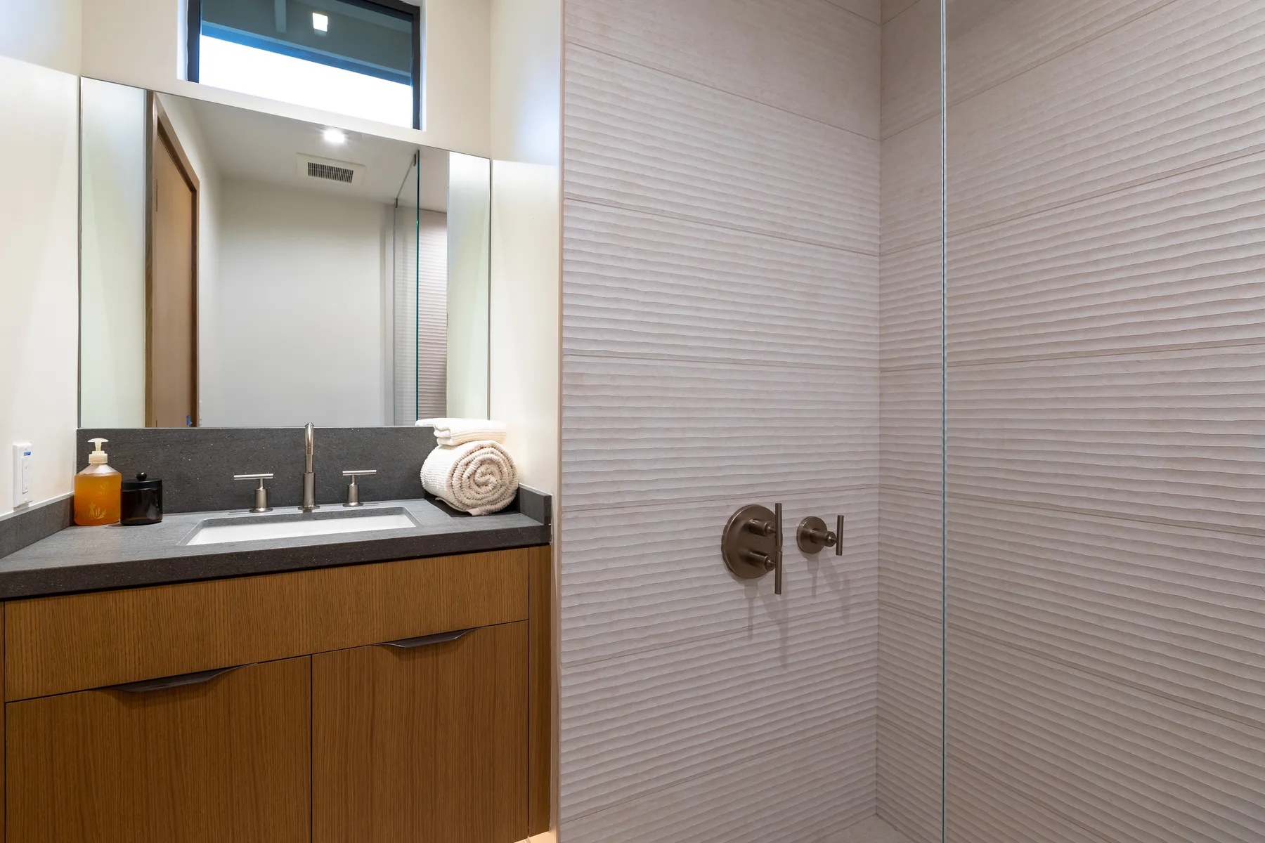 A modern bathroom with a wood vanity, wide mirror, and tiled shower.