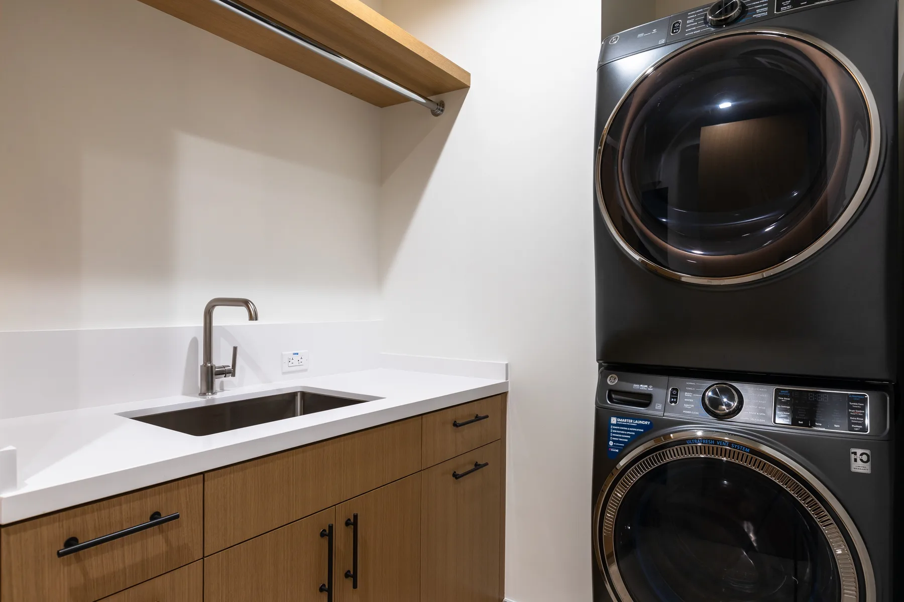A laundry area with a stacked washer and dryer beside a sink and countertop.