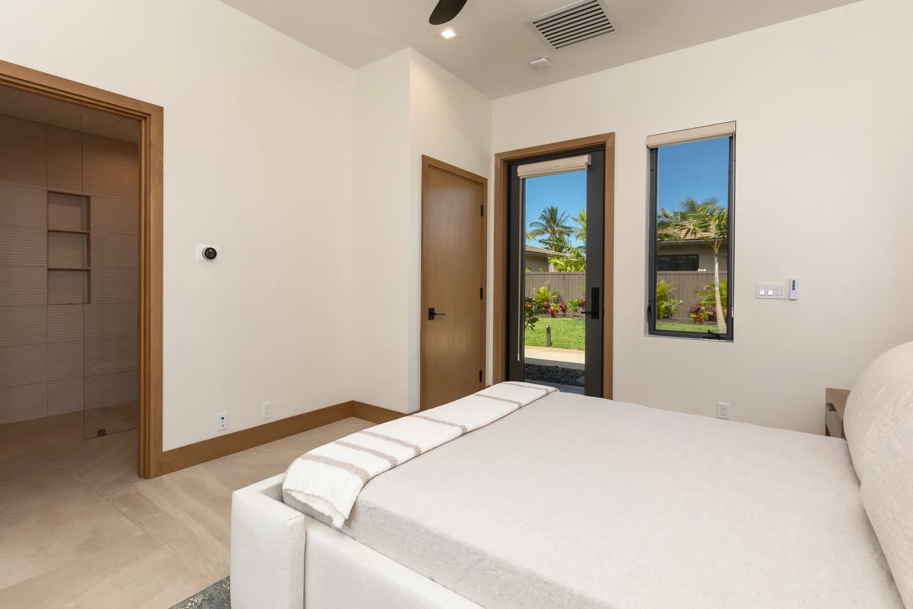A bright bedroom with a large bed and glass doors opening to a garden.