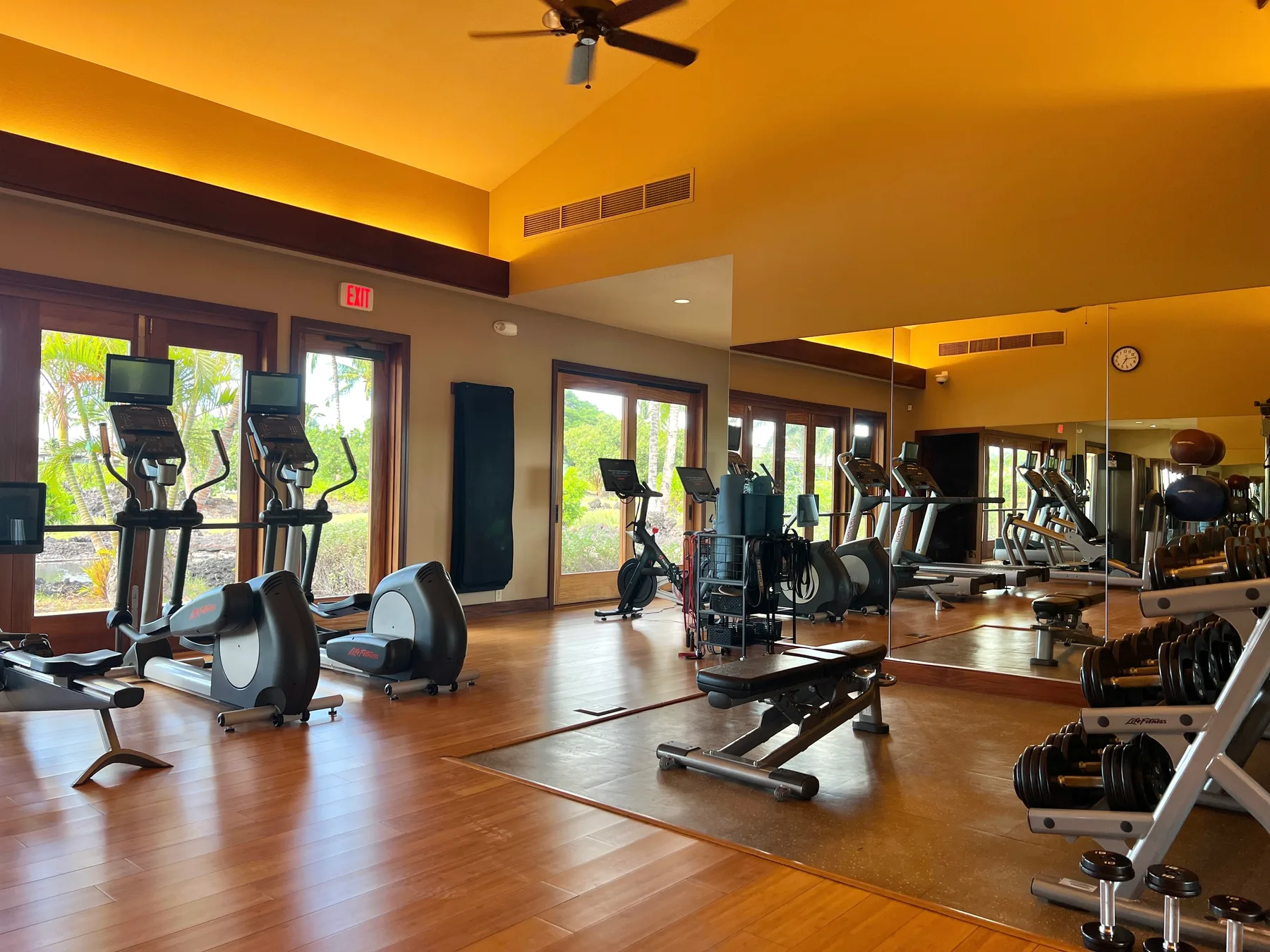 A gym with exercise machines and weights arranged across a wood-floored room.