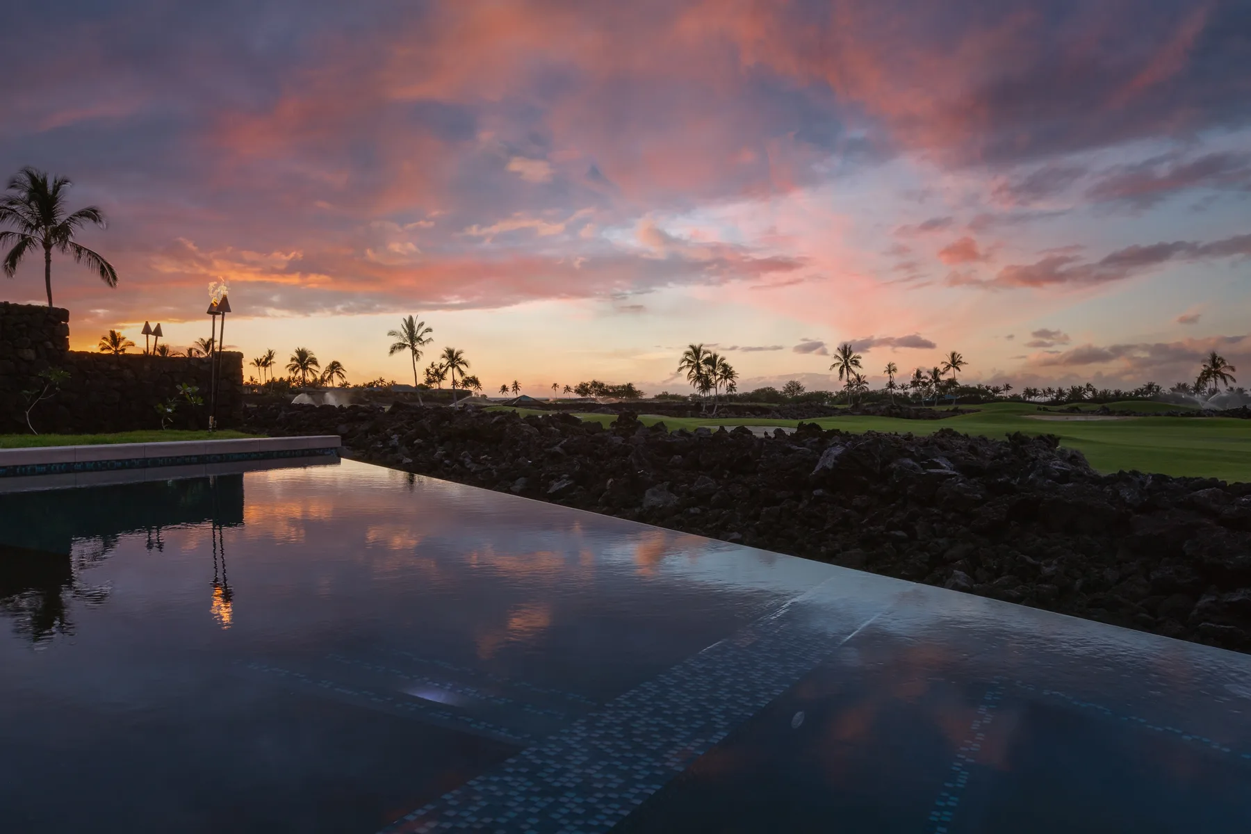A reflecting pool overlooks a palm-lined landscape beneath a colorful sunset sky.