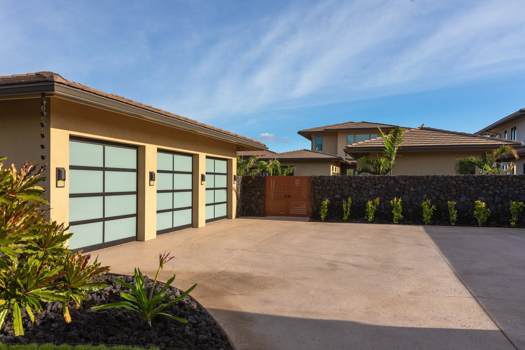 A paved driveway beside a garage, with a low stone wall and gate.