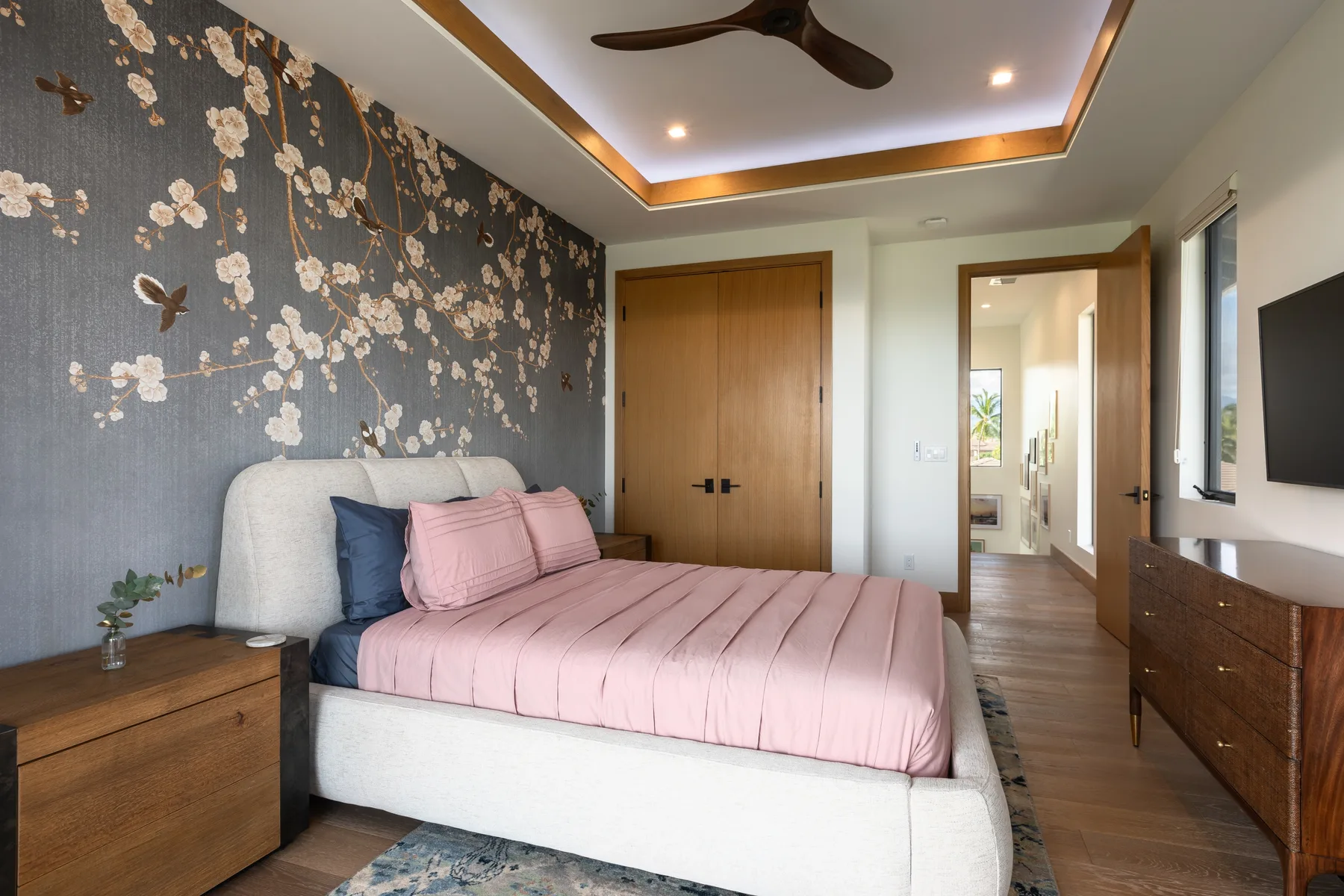 A bedroom with a bed dressed in pink bedding beside a floral-patterned wall.