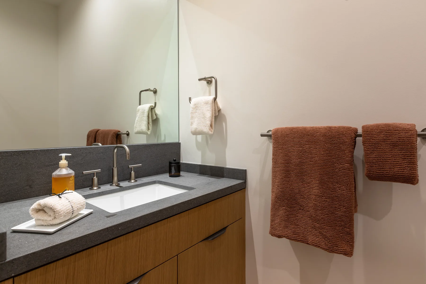 A bathroom vanity with a sink, large mirror, and brown towels hanging nearby.