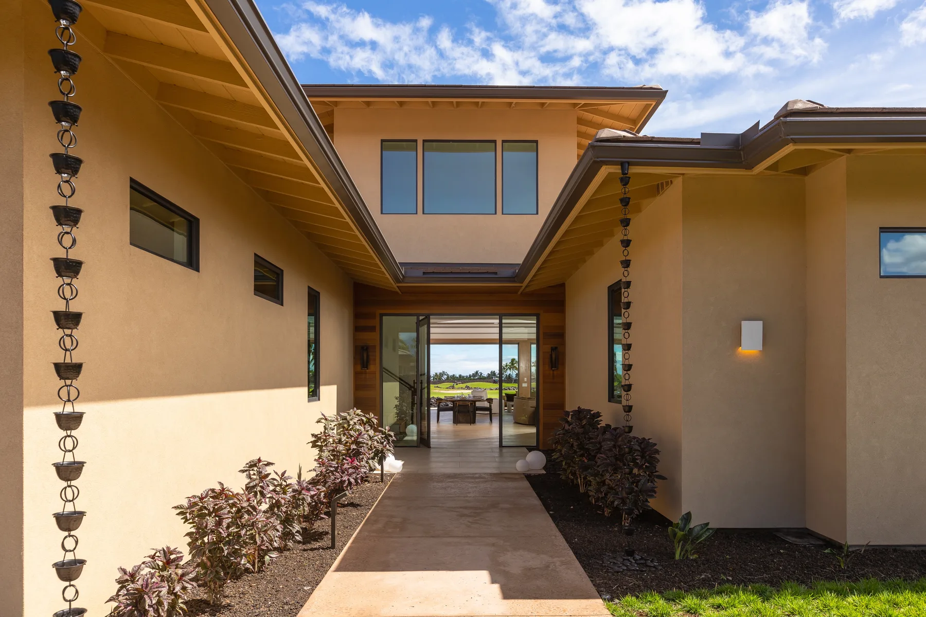 A covered courtyard walkway leads toward a glass doorway between tan stucco walls.