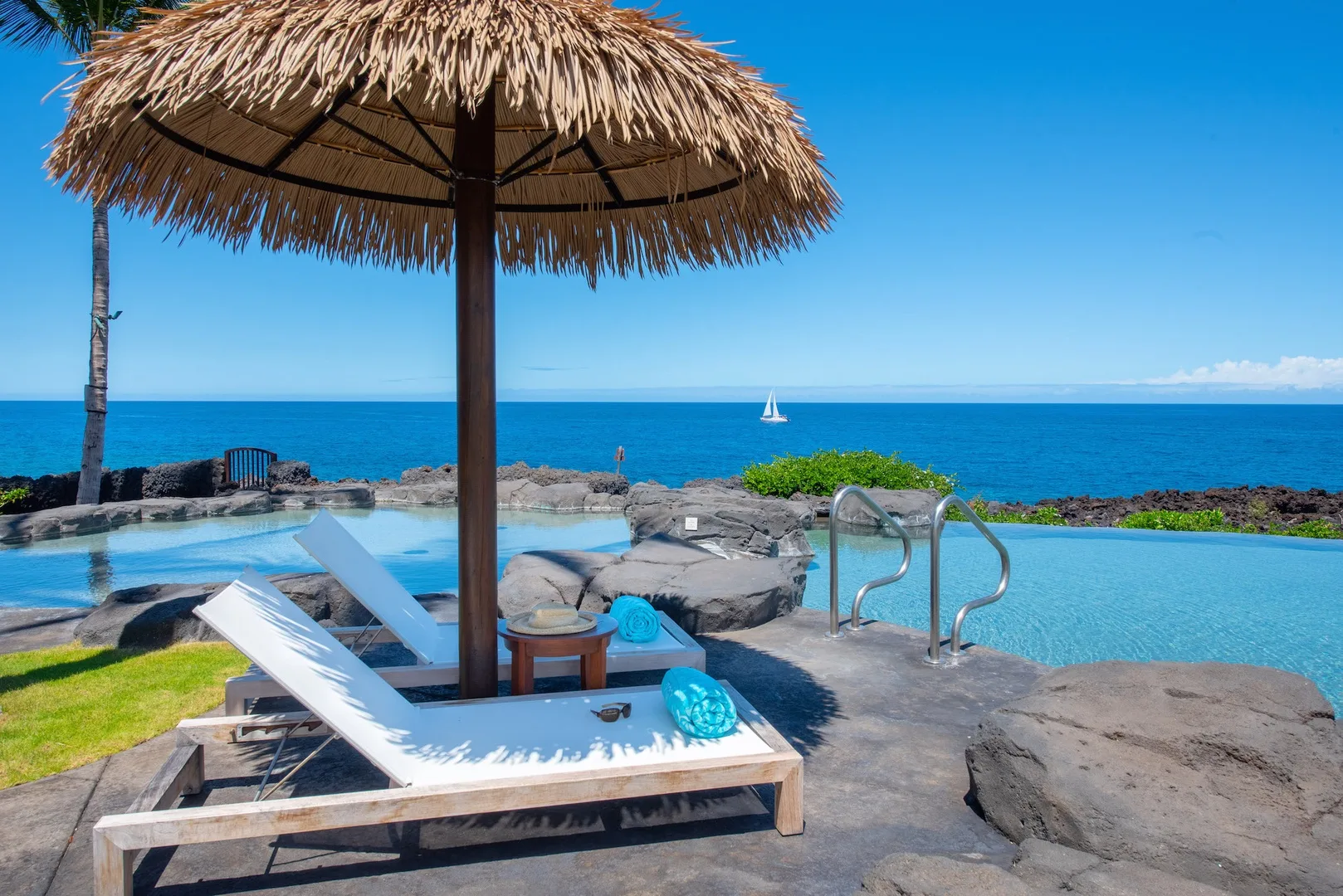 An oceanfront pool with a thatched parasol and lounge seating overlooks the sea.