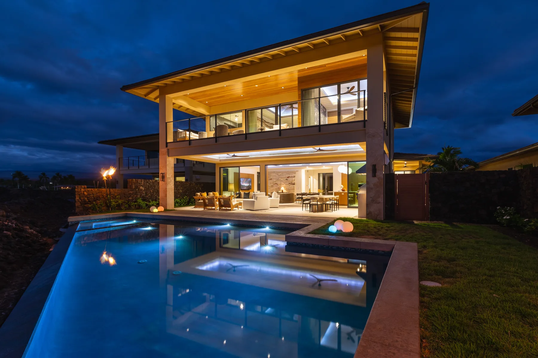 Una casa moderna de dos plantas brilla al anochecer junto a una piscina iluminada.