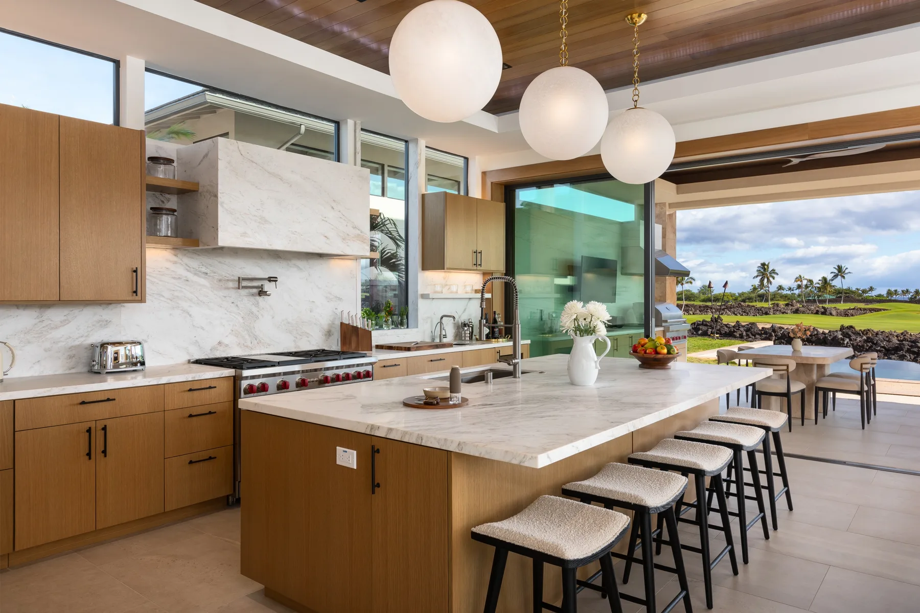 A modern kitchen with a large island and windows overlooking palm trees.