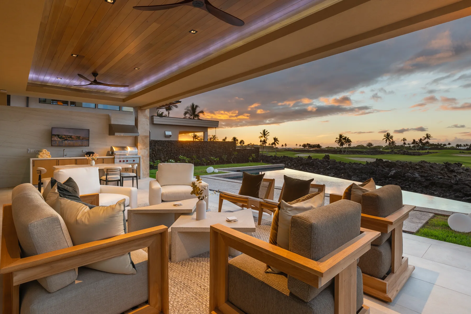 Una sala exterior cubierta con asientos da a un jardín al atardecer.