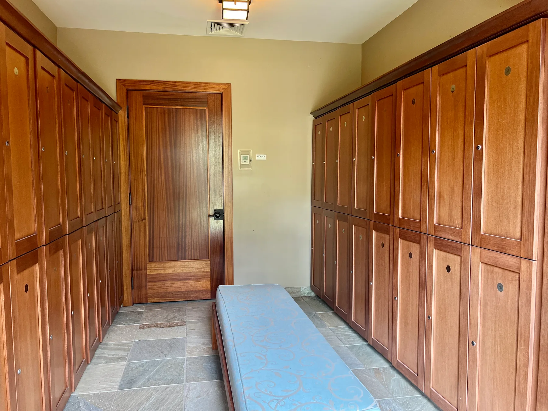 A locker room with wooden lockers lining the walls and a bench in the center.