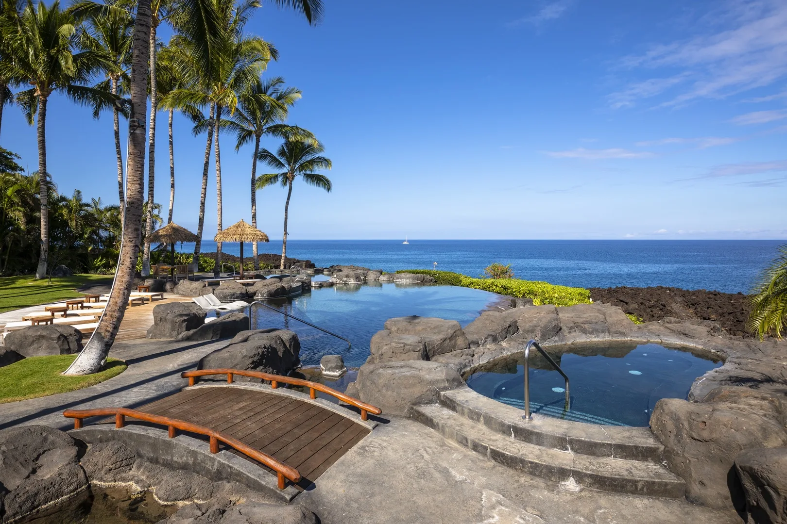 A rocky seaside pool sits beside palm trees and the ocean.